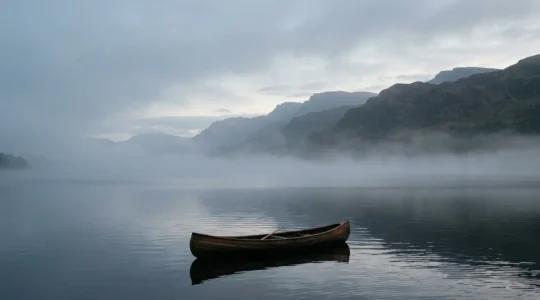 Atmospheric view of a canoe at dawn on misty Scottish loch with mountains reflected in still water