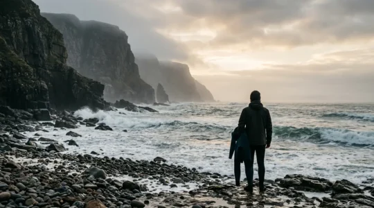 Scottish surfer preparing wetsuit at dawn on rugged Highland beach with dramatic cliffs